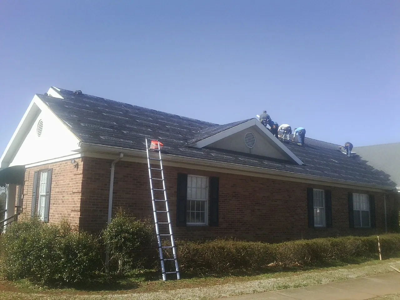 Crew tearing shingles off a brick ranch roof with a ladder set — Emergency Roof Repair work by our crew in Coos Bay