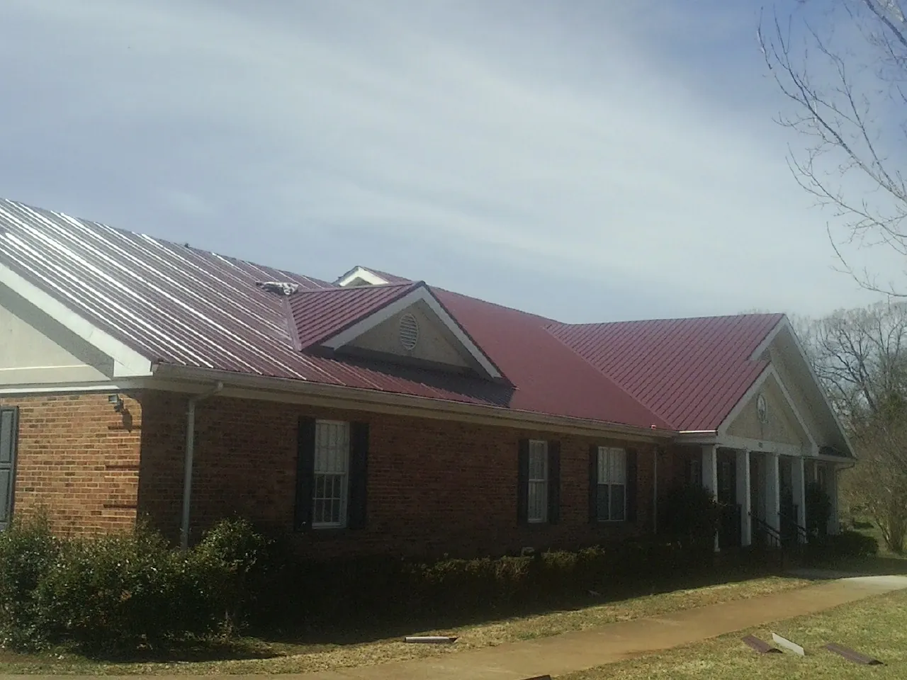 Red metal roof with gabled entries on a long brick building, from a Hail Damage Roof Repair job in Coos Bay