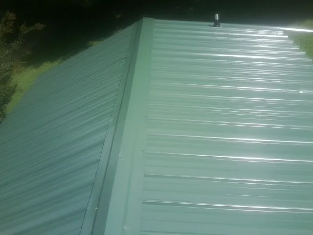 New green metal panels meeting at the ridge of a roof — Flat Roof Repair work by our crew in Coos Bay