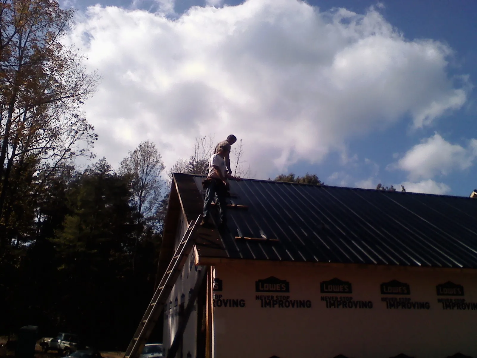 Roofer fastening dark metal panels high against a cloudy sky, from a Roof Inspection job in Coos Bay