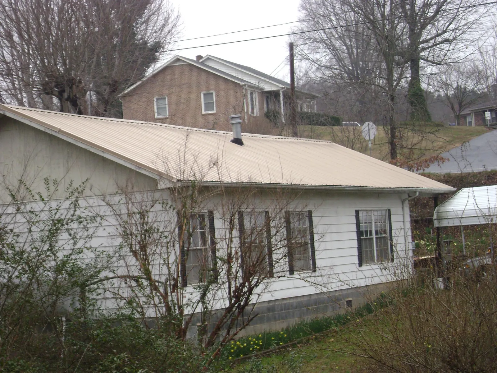 Tan metal roof on a white sided house set into a hillside — Commercial Roofing by Roofing Brothers in Coos Bay